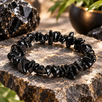 Bracelet en obsidienne noire posé en cercle sur une pierre claire, détail des perles chips brillantes