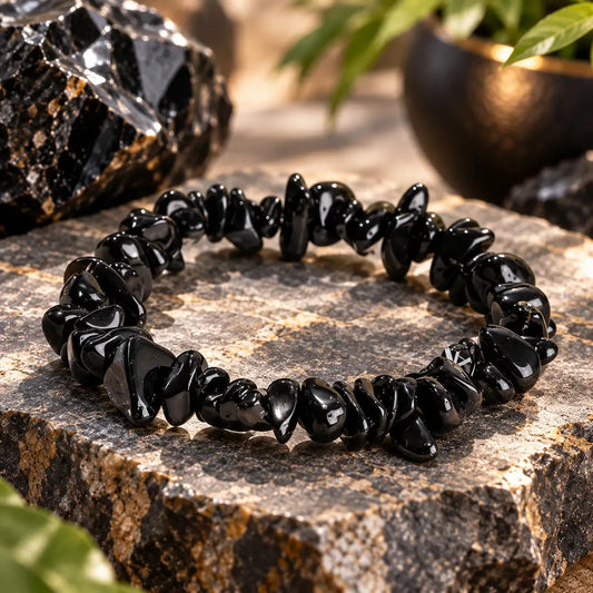 Bracelet en obsidienne noire posé en cercle sur une pierre claire, détail des perles chips brillantes