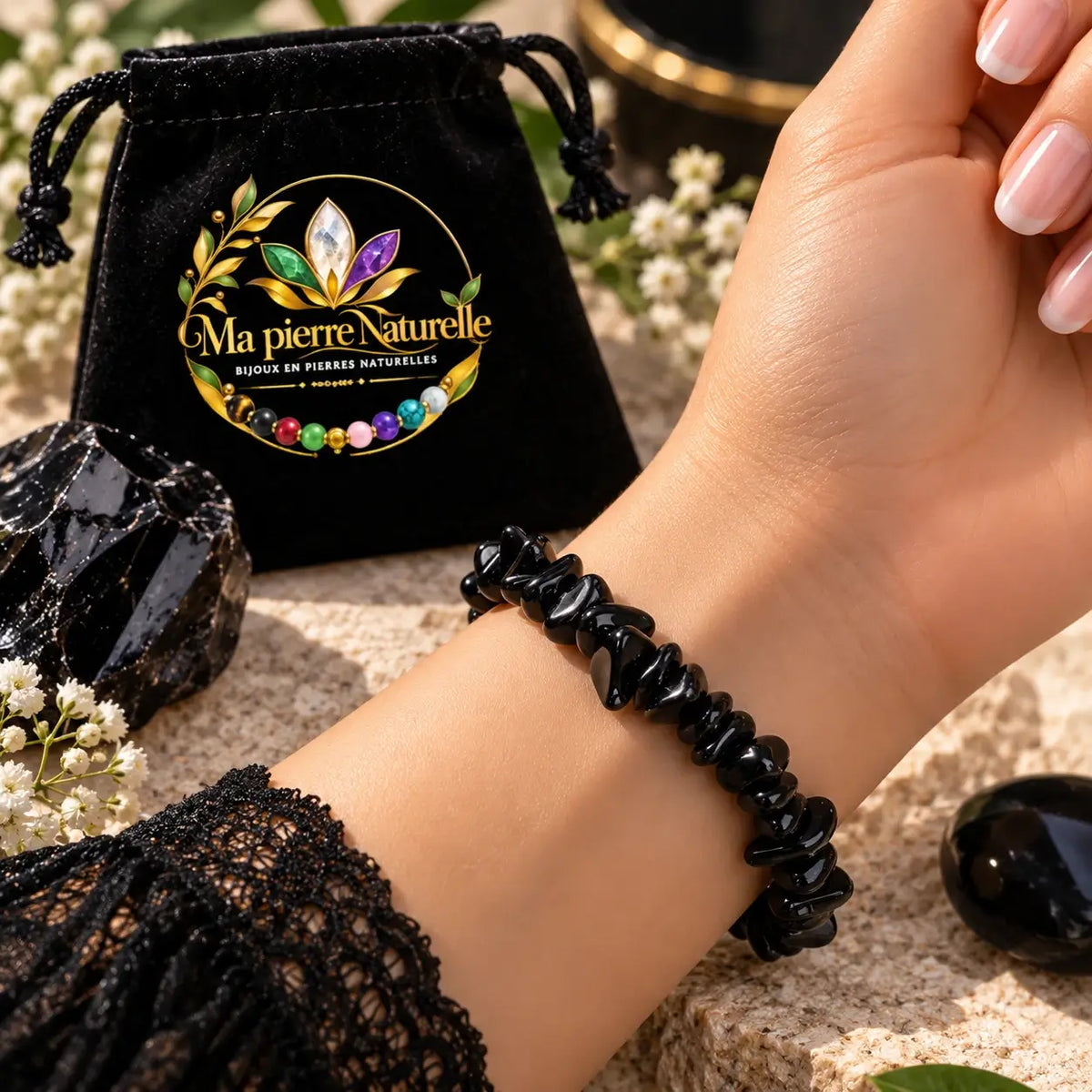 Bracelet en obsidienne noire porté au poignet avec une manche en dentelle noire et une pochette en arrière-plan