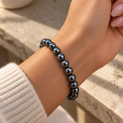 Bracelet en hématite de 8 mm à l’éclat métallique, porté au poignet avec une manche claire.