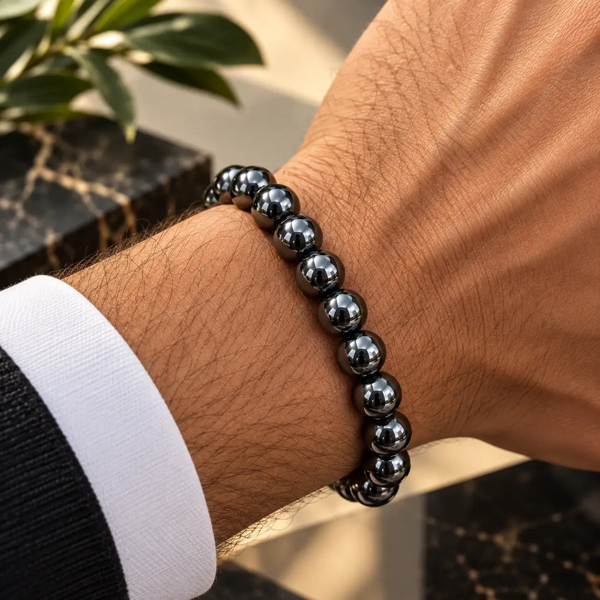 Bracelet en hématite gris anthracite de 8 mm porté au poignet avec une manche foncée.